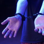 Close-up of pale hands in metal handcuffs in a dimly lit setting.